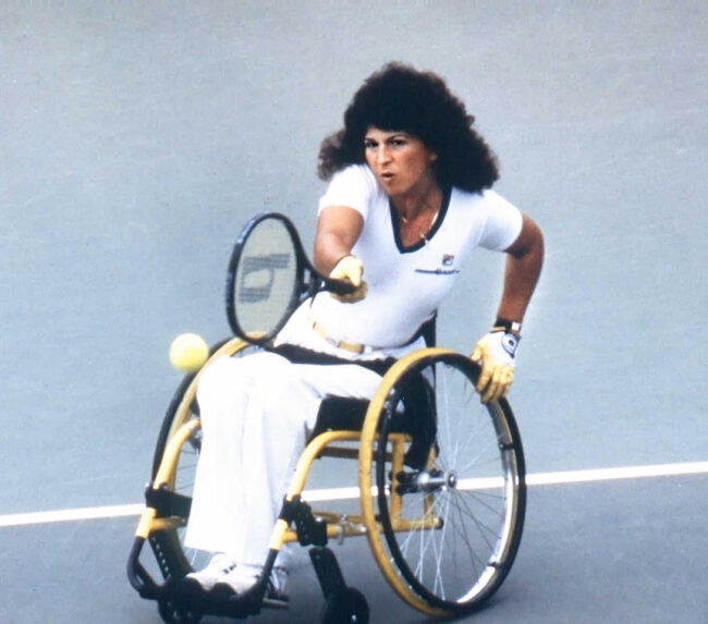 Marilyn Hamilton on the court hitting a tennis ball in match from her wheelchair