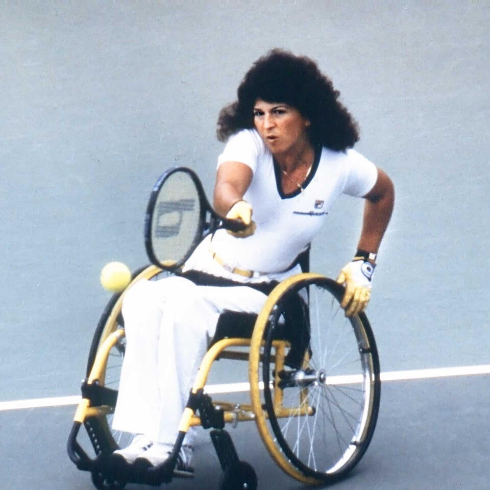 Marilyn Hamilton on the court hitting a tennis ball in match from her wheelchair